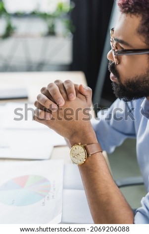 Side view of african american businessman in eyeglasses sitting near blurred papers in office