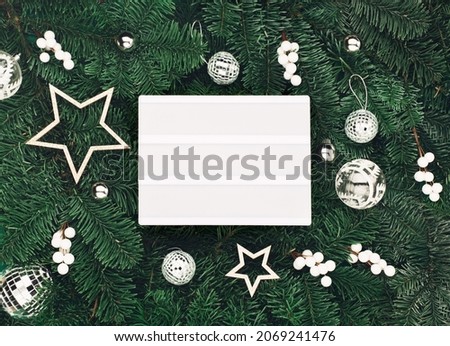 Empty white Lightbox with holiday silver and white decorations, acorns on green Christmas tree branches background. Flat lay, top view, copy space. Festive Winter time.