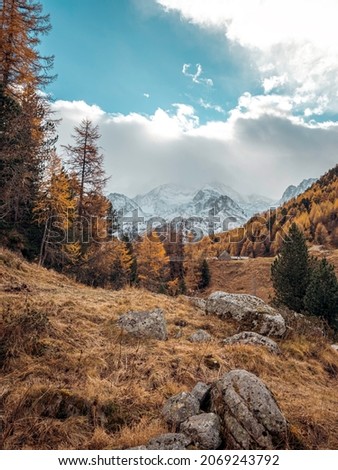 Amazing views over an high alpine valley and snow covered mountains. Orange and yellow coloured autumn and fall trees line the valley sides as the peaks rise above the clouds.