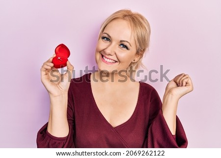 Young blonde woman wearing engagement ring screaming proud, celebrating victory and success very excited with raised arm 