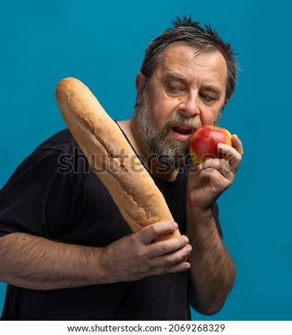 Healthy lifestyle concept. Hard choise. What is better bread or vegetables. A middle-aged man in a black T-shirt holds vegetables in one hand and bread in the other