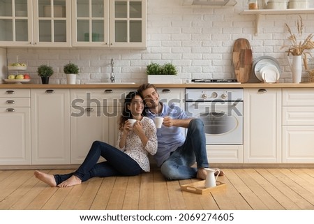 Homeowners family couple in love relax on wooden warm floor in kitchen holds cups drinking tea or morning coffee beverage enjoy daydream together at new own or rented house. Tenancy, bank loan concept Royalty-Free Stock Photo #2069274605