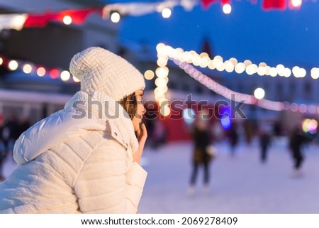 Christmas, winter and leisure concept - happy young woman near ice skating rink outdoors.