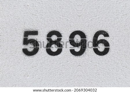 Black Number 5896 on the white wall. Spray paint. Number five thousand eight hundred ninety six.