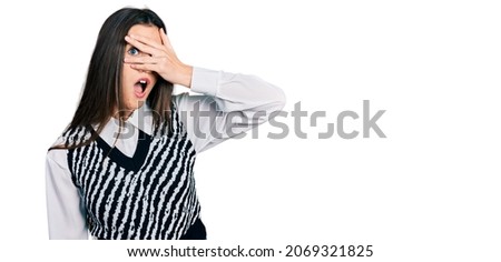 Young brunette teenager wearing casual elegant look peeking in shock covering face and eyes with hand, looking through fingers afraid 
