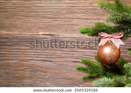 Sparkling Christmas bauble with pink bow hanging on Christmas tree branch against wooden background with copy space, Holiday concept space for text