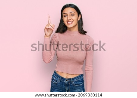 Young hispanic girl wearing casual clothes showing and pointing up with finger number one while smiling confident and happy. 