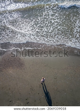Aerial view from a drone of a man in swimming trunks standing on the seashore.Hot beach with cool waves.Concept of summer and relaxation, seascape with a man, beach, beautiful waves