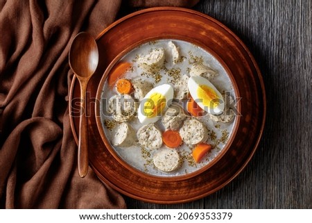 Zurek polish fermented rye soup with traditional polish white kielbasa or sausage with marjoram, hard-boiled eggs served on a clay bowl with a wooden spoon, on a dark wooden background, top view