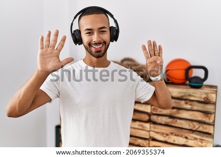 African american man listening to music using headphones at the gym showing and pointing up with fingers number nine while smiling confident and happy. 