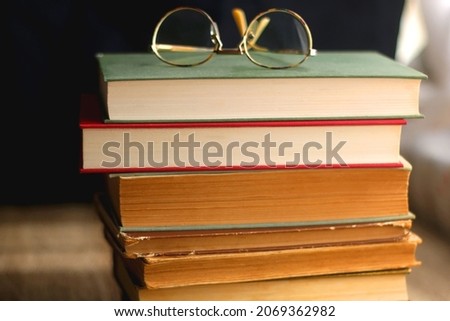 Stack of hardcover books and reading glasses. Selective focus.