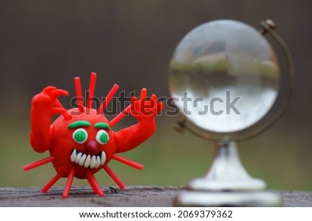 A virus figurine threatens a glass globe. A symbolic image of the coronavirus.