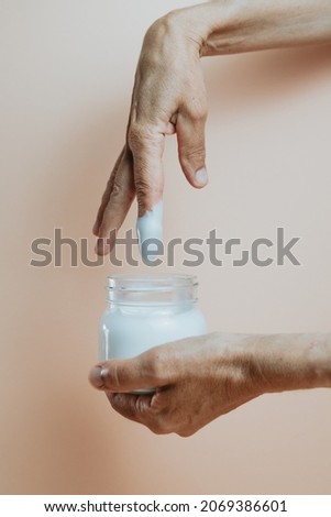Old hands taking body lotion cream from a bottle, minimalist shot, pastel colour background