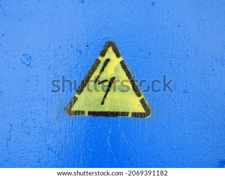 
Yellow and black high voltage sign on a bright blue background. Depicted using a stencil.					