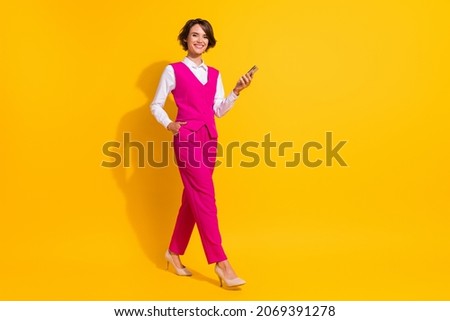 Photo of charming shiny young lady wear pink suit smiling walking typing modern device empty space isolated yellow color background