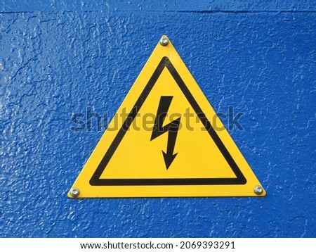 
Metallic bright yellow high voltage sign on a blue wall. Beautiful abstract image.					