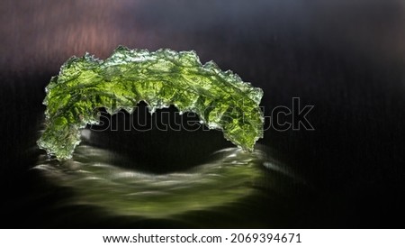 Green moldavite jewel in arch shape on black background with beautiful reflection and mystery glow. Closeup of rare gemstone of meteoric glass in artistic still life. Mineral collecting. Czech origin.