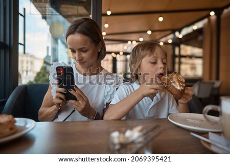Mother and son having lunch in sidewalk restaurant.Mom and son eat a croissant in a cafe.Woman photographing food. 