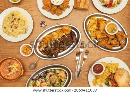 selection of international dishes, gnocchi with cheese and nuts, grilled beef, hamburger with potatoes, breaded chicken strips, prawn cocktail, forks