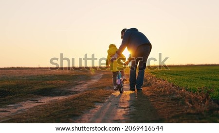 Father teaches a little kid girl to ride a child's bike on the road, in the fall, in spring. Happy family, childhood. Happy family, dad teaches his daughter, child to ride a bike in the park at sunset Royalty-Free Stock Photo #2069416544