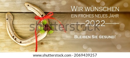 golden horseshoe with red ribbon and shamrock with german text who means good wishes for the new year 2022