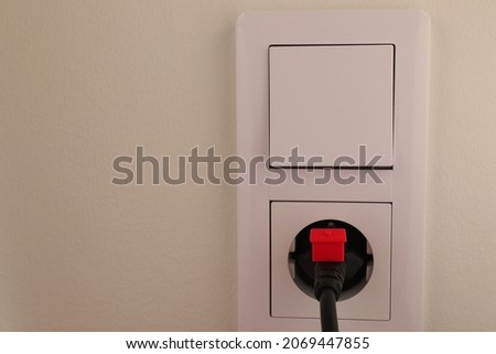 A white power outlet or socket. Tiny red house. Concept of expensive electricity. Close up and isolated. Stockholm, Sweden.