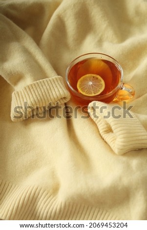 Cup of hot tea and cashmere yellow sweater on a bed. Concept of cozy and warm home.
