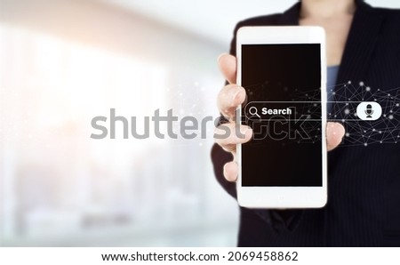 Data Search Technology Search Engine Optimization. Hand hold white smartphone with digital hologram search data sign on light blurred background. Minimal blank search bar with voice command.