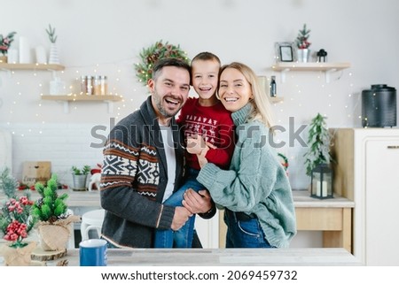 A young family with a son in the kitchen rejoice in the holidays, a husband and wife and a little boy have fun together hugging and playing on New Year's and Christmas holidays
