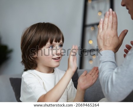 Smiling male kid rejoicing hitting palm clapping hands to woman nanny playing together. Cheerful boy child enjoying happy childhood spending time with mother at home weekend entertainment activity