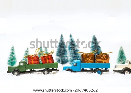 Miniature transport trucks loaded with Christmas packages in a snowy landscape with spruce trees. white background with copy space