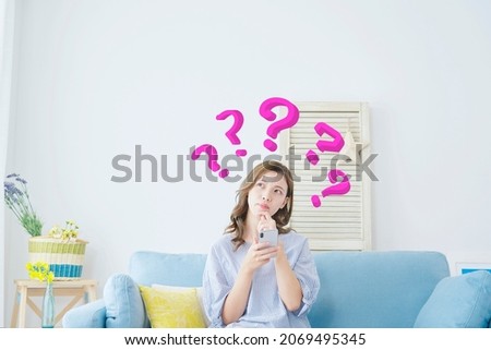 Asian woman thinking with the smartphone at home Royalty-Free Stock Photo #2069495345