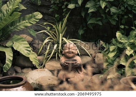 E Statuette figurine symbol brown stone buddha smile hold bowl. Copy space nature tropical leaves plants garden. Mysterious calm soul meditation mood buddhist culture. Bright green, more tone in stock