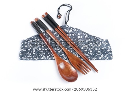 A pair of wooden spoon, fork, and chopsticks with a rope wrapped around the handle placed on a Japanese-style leaf and flower patterned cloth wrapping isolated on white background. Top view. Close up.