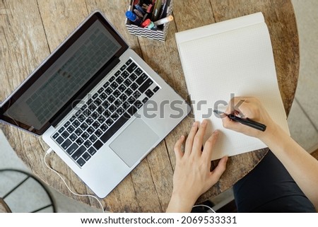 Online studying concept a black-haired student doing his homework by searching information on the internet and using this black pen to write the conclusion of his research on the paper. Royalty-Free Stock Photo #2069533331