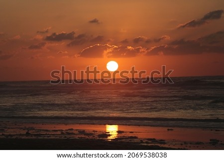 This is a picture of a sunset on the beach with cloudy sky and orange color.