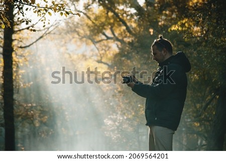 photographer takes pictures of autumn landscape in early morning in fog and rays of sun. Morning haze in autumn forest.