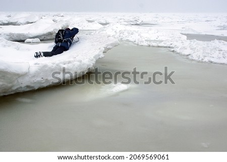The photographer lies on a dangerous ledge of ice in early spring during the ice melting.