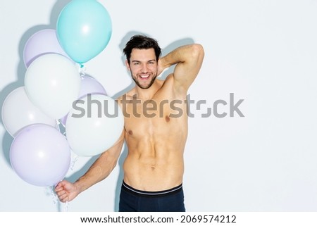 Funny Laughing Caucasian Handsome Brunet Man With Bunch of Colorful Air Balloons in Hand While Posing in Underware Against White Background. Horizontal Image