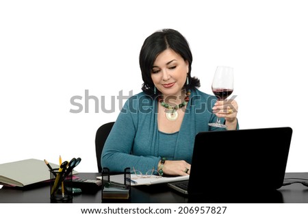 Attractive female freelancer surfing favorite websites on her laptop. Middle aged woman sits at the desk and enjoying a glass of red wine after a long working day