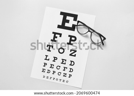 Stylish eyeglasses with eye test chart on light background Royalty-Free Stock Photo #2069600474