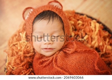 Close up Baby newborn wearing fox mohair bonnet and orange brown swaddling wrap sleeping with smile on wool yarn with wood background.
