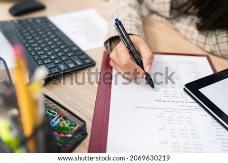 Close-up on a document, statistical table, company's calculations, an office accountant sits at the desk filling in the right places, checking the correctness, touches the paper with a pen