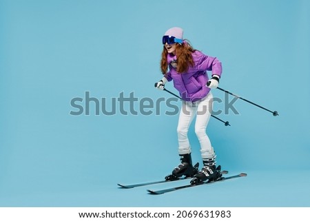 Full body skier smiling happy fun cool woman 20s wearing warm purple padded windbreaker jacket ski goggles mask spend extreme weekend in mountains look camera isolated on plain blue background studio.