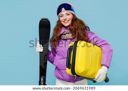 Traveler happy tourist woman in ski windbreaker jacket goggles hold valise suitacase isolated on plain blue background studio Passenger travel abroad on weekends getaway Air flight journey concept.