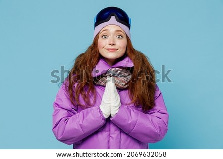 Skier woman in warm purple padded windbreaker jacket ski goggles mask spend extreme weekend in mountains hands folded in prayer gesture beg about something isolated on plain blue background studio.