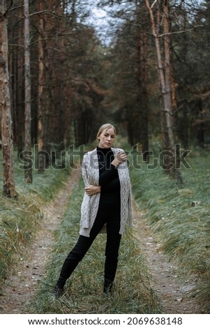 girl in a gray cape and black dress among the autumn forest
