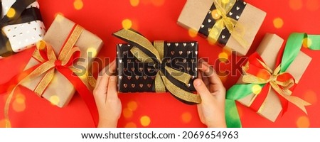 Kids hands holding decorativegift box with bow on red background. Sale, Holiday, greering card Happy new year 2022, Merry Christmas, banner for your site, invitation, flyer, holiday invitation