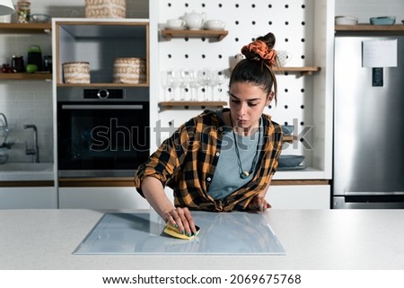 Young beautiful woman suffers from depression after breakup or divorce and suffers from OCD cleans kitchen cook top to calm her nerves. Obsessive compulsive disorder female rubbing the with sponge.