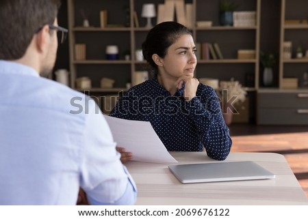 Unhappy young Indian job seeker holding paper document in hands, thinking on offer, feeling dissatisfied with career opportunities. Confused hr manager having bad first impression at interview. Royalty-Free Stock Photo #2069676122